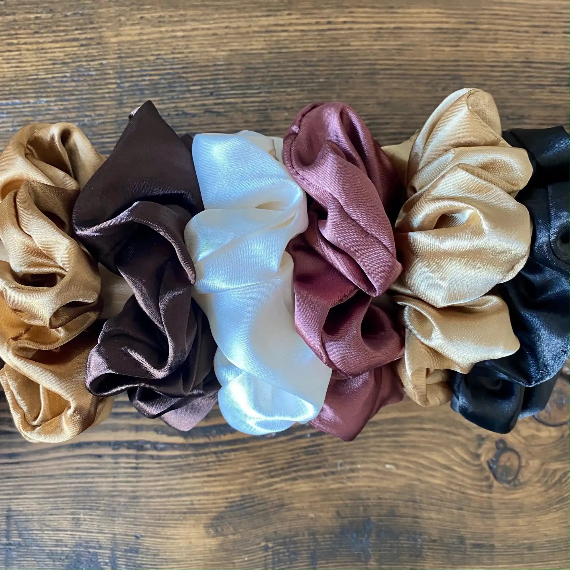 Une rangée de scrunchies en soie de différentes couleurs, y compris or, marron, crème, rose et noir.